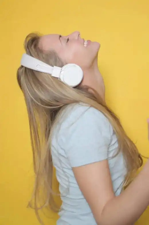 A woman with blonde hair wearing white over-ear headphones and a light blue t-shirt.